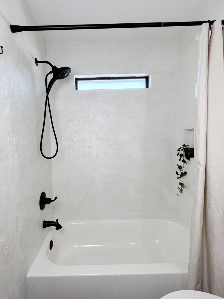 Completed DIY microcement bathroom with bathtub, shower niche, and black fixtures.