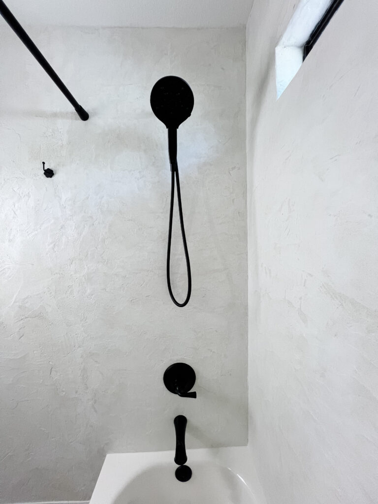 Black shower fixtures installed on seamless white microcement walls.