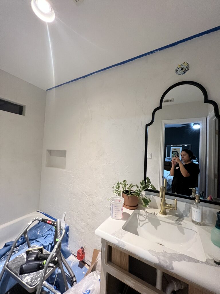DIY microcement bathroom project in progress with white textured walls, vanity sink, and arched mirror.