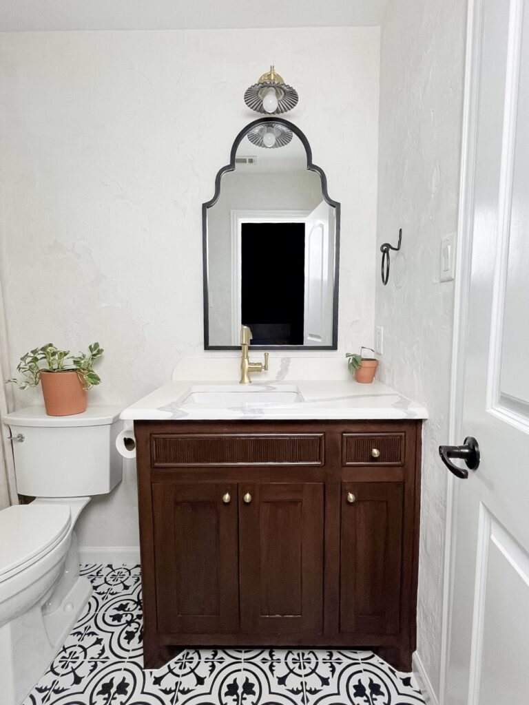 Completed DIY microcement bathroom with dark wood vanity, gold faucet, and arched mirror.