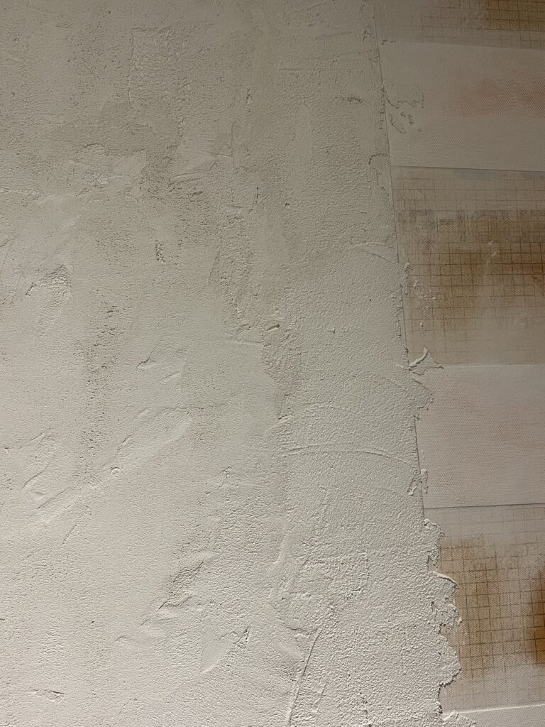 First coat of microcement applied over Kerdi board shower wall showing rough textured surface.