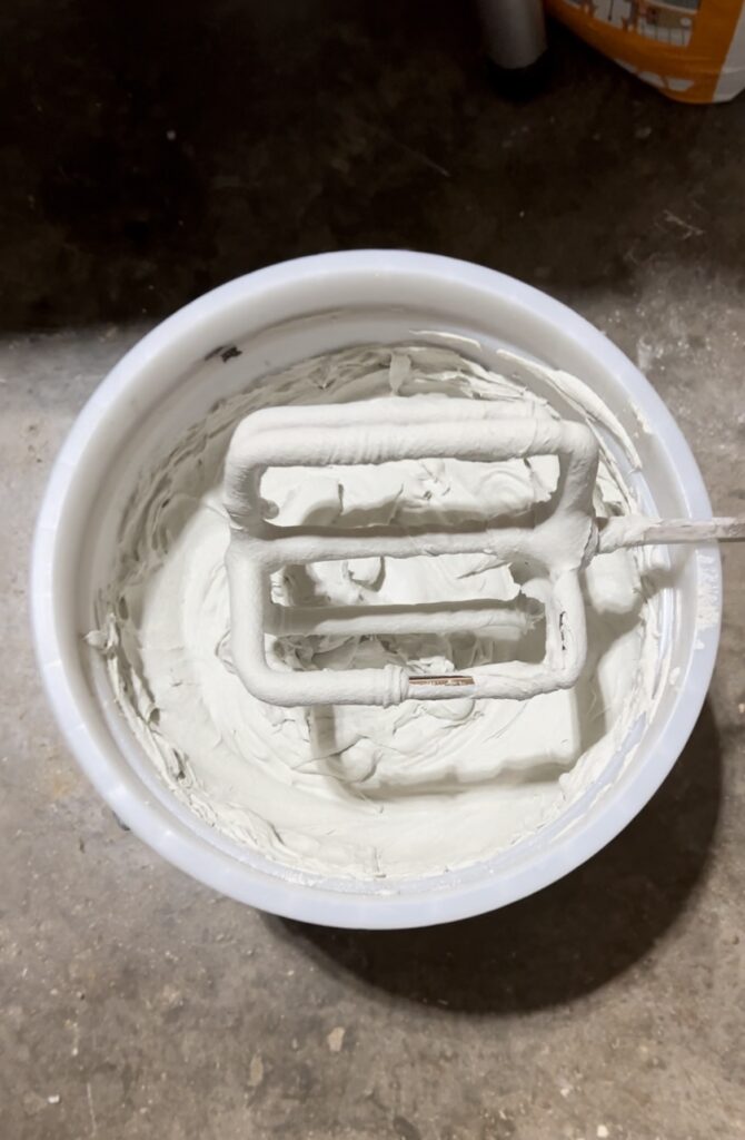 Freshly mixed white microcement in a bucket with a drill mixing attachment during DIY renovation.