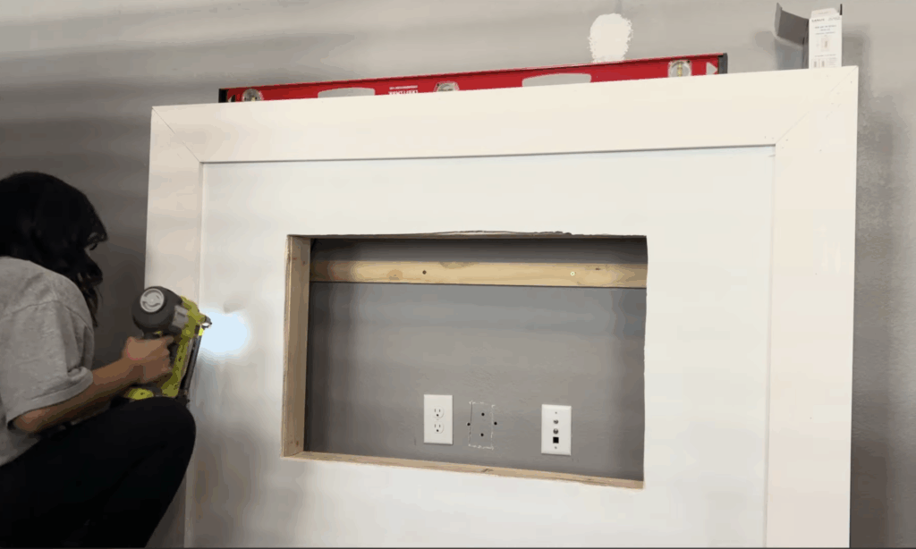 Nailing white trim boards around the drywall fireplace opening using a brad nailer for a clean, built-in look.