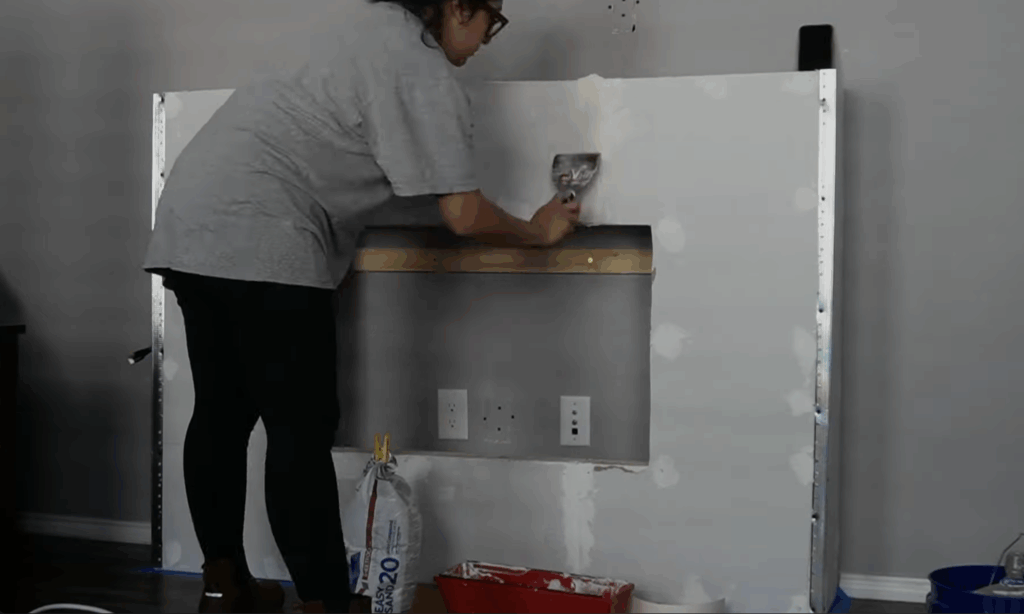 Smoothing joint compound over drywall seams of the DIY fireplace wall using a taping knife.