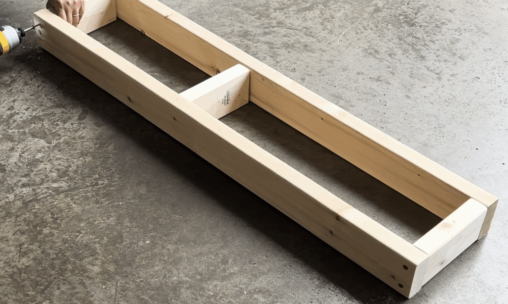 Assembling the base frame for the DIY electric fireplace using 2x4 lumber on a garage floor.
