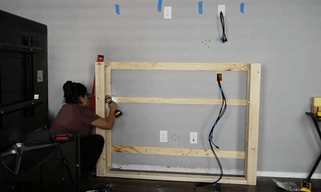 Attaching vertical 2x4 supports to complete the basic wood frame for a DIY electric fireplace build.