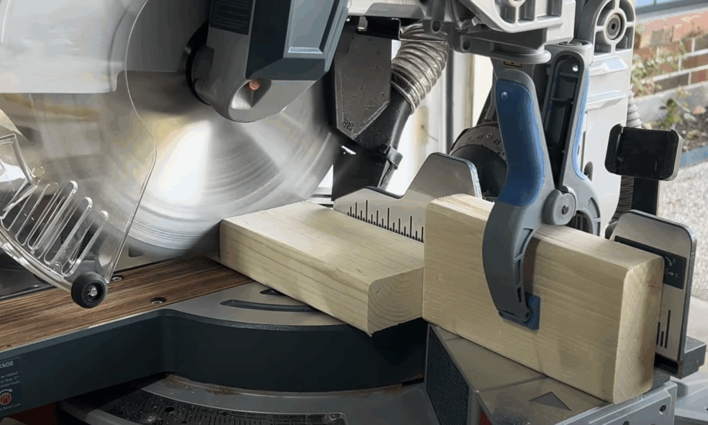 Cutting 2x4 lumber to size with a Bosch miter saw while preparing materials for the DIY electric fireplace frame.