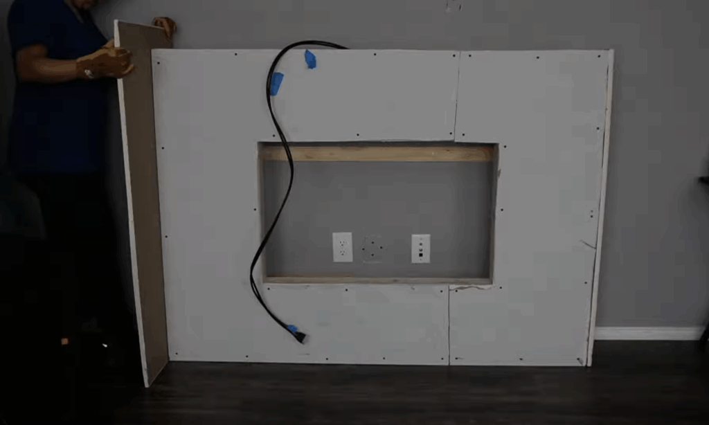 Cutting and fitting fire-rated drywall around the opening for an electric fireplace insert.