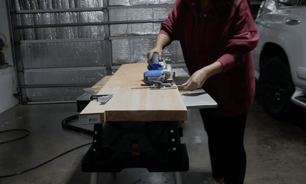 Cutting a wooden mantel to size using a blue Kobalt circular saw on a garage workbench.
