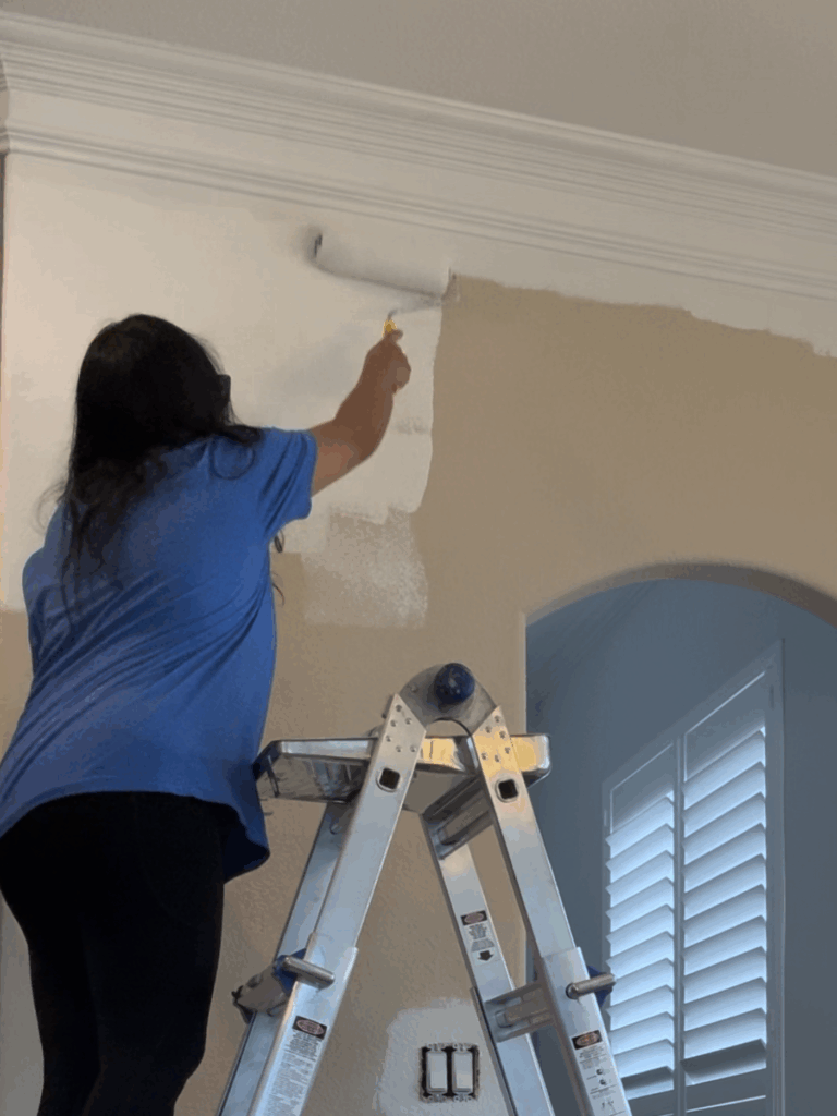DIY homeowner using a roller to paint over beige kitchen walls with fresh white paint during a budget kitchen glow up.
