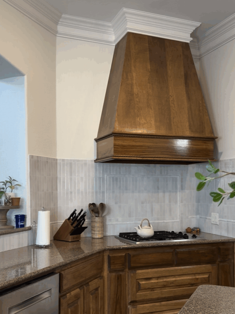 Updated kitchen corner with wooden vent hood, new peel-and-stick backsplash, and bright white painted walls
