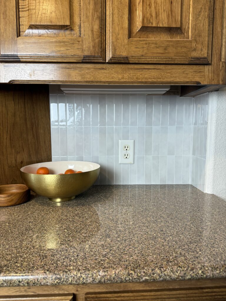 Corner of refreshed kitchen countertop with gold fruit bowl, modern backsplash, and clean painted walls.
