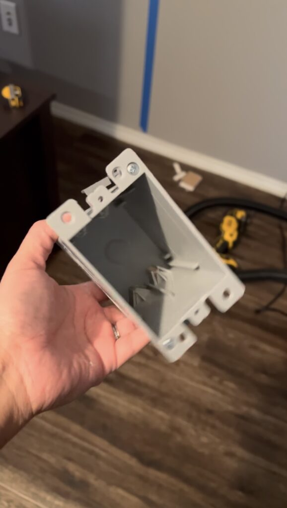 Holding a plastic old-work electrical box before installation as part of the DIY electric fireplace wiring setup.