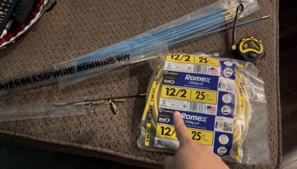 Romex 12/2 wire, fish stick kit, and tape measure laid out for running electrical wiring for the DIY electric fireplace.