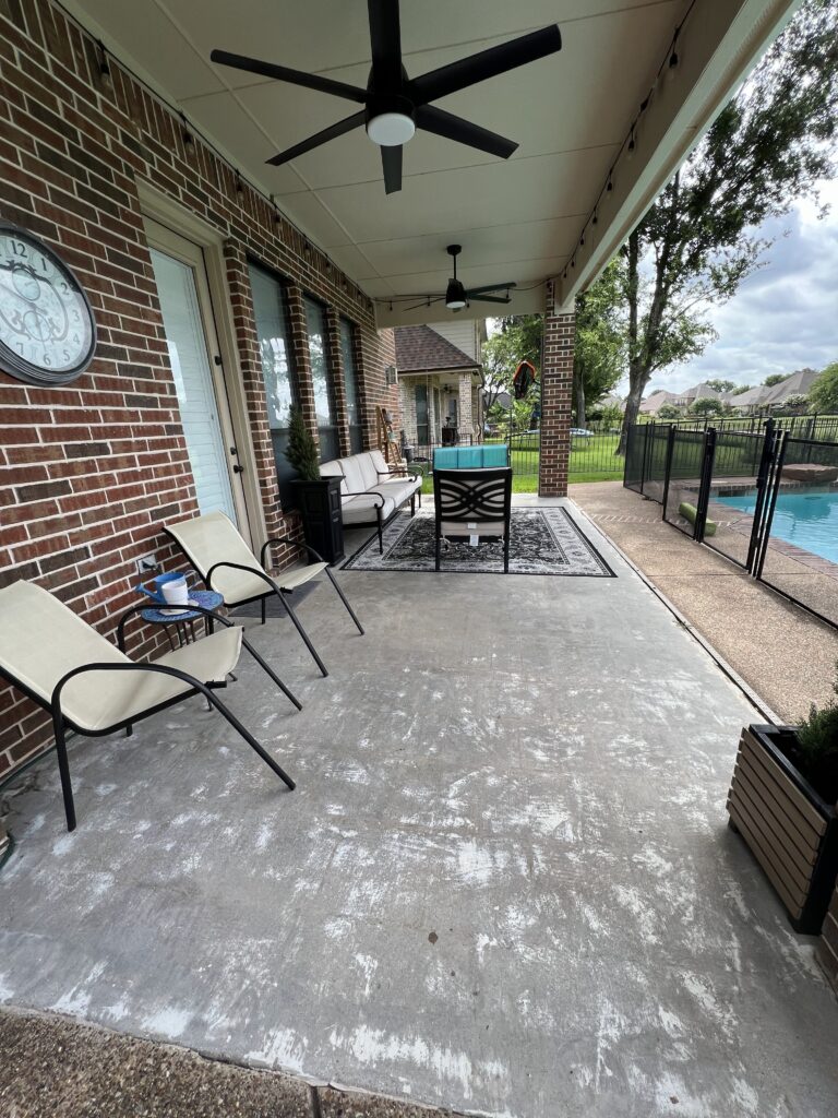 Bare concrete patio before painting, with outdoor chairs and a rug near the pool.