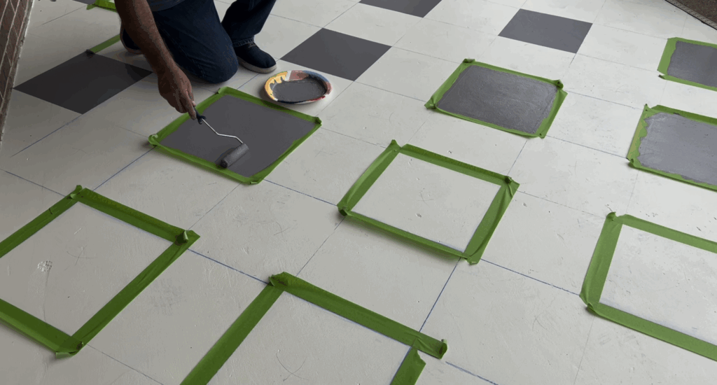 Gray paint being rolled into taped-off squares using green Frog Tape for clean edges.