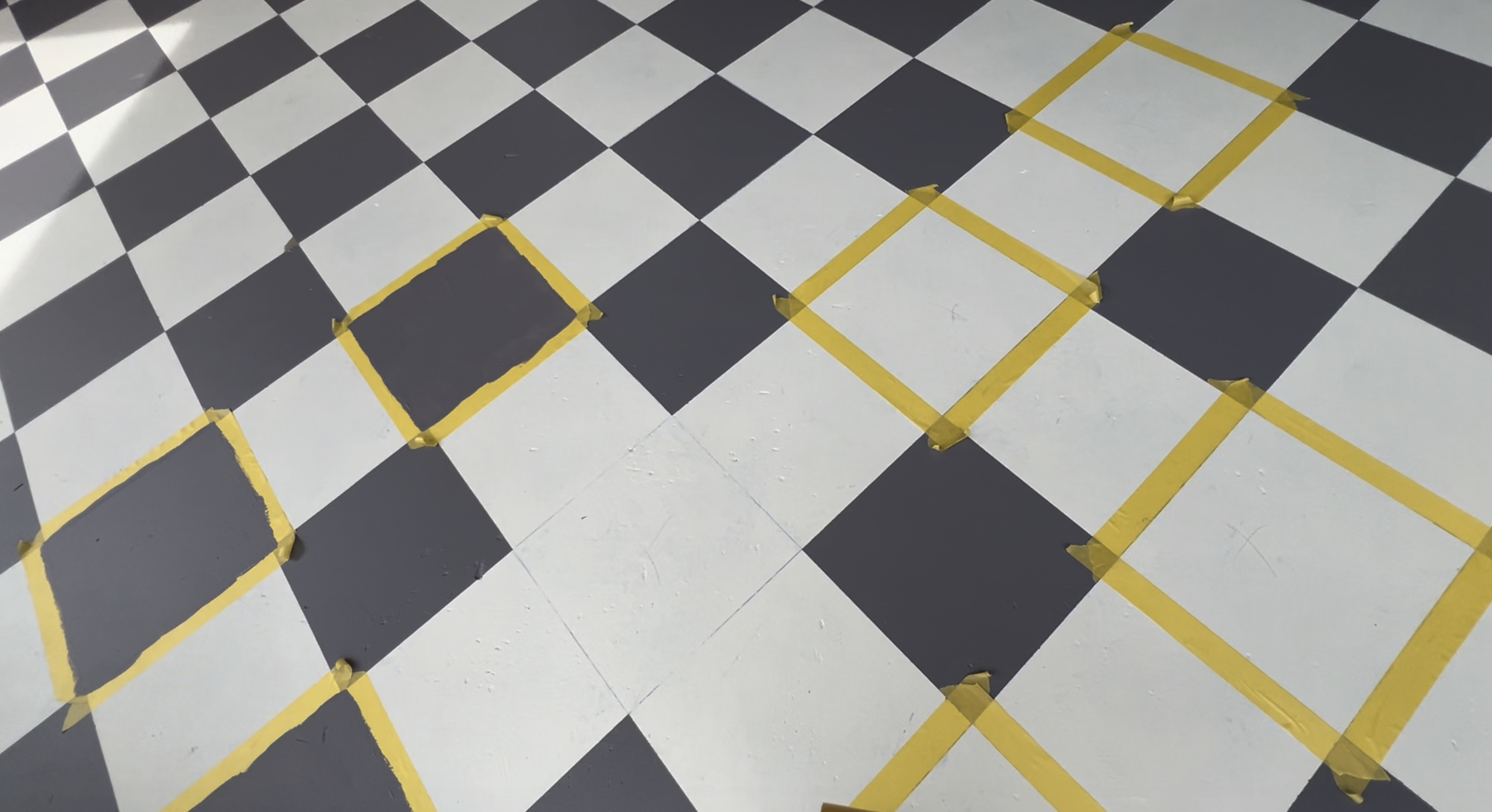 Yellow Frog Tape marking off individual squares across the painted checkered patio.