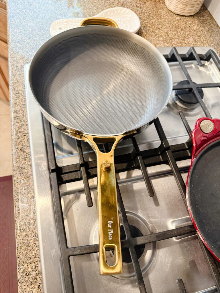 Our Place titanium nonstick pan with gold handle heating on a gas stovetop