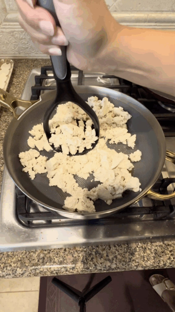 Firm tofu being crumbled and cooked in a pan for a vegan breakfast burrito