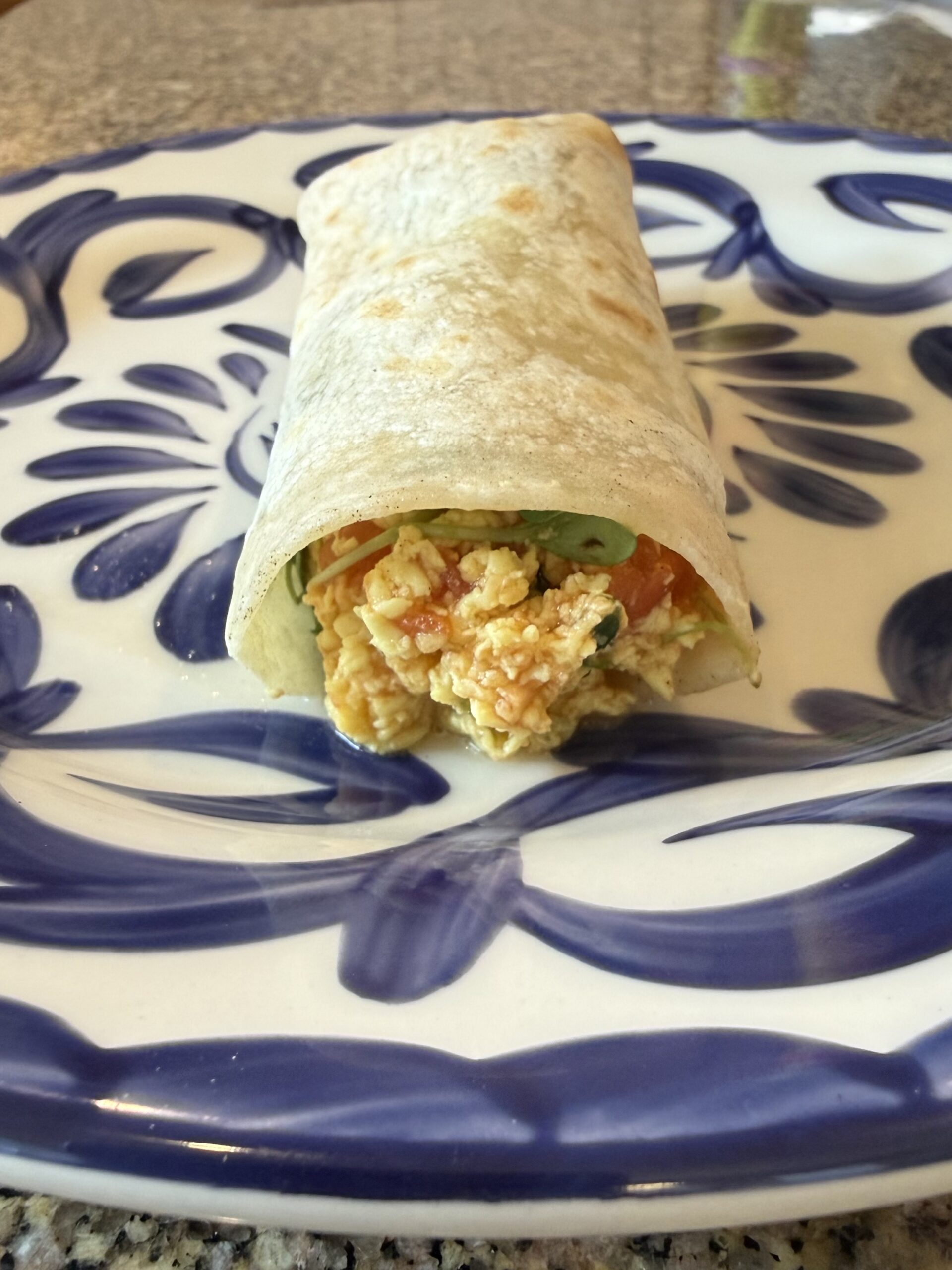 Vegan breakfast burrito filled with tofu scramble, vegetables, and salsa on a blue and white plate
