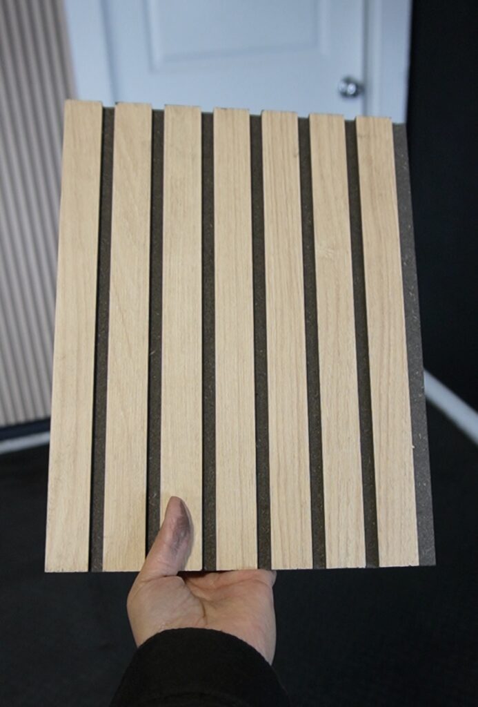 Close-up of a fluted MDF wall panel from Lowe's showing warm oak finish and deep black slat detail