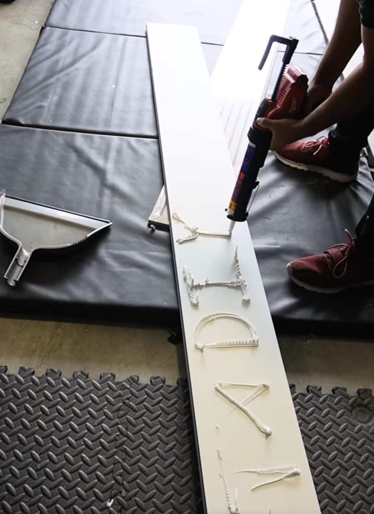 Applying Liquid Nails construction adhesive to the back of a fluted MDF panel before installing on wall