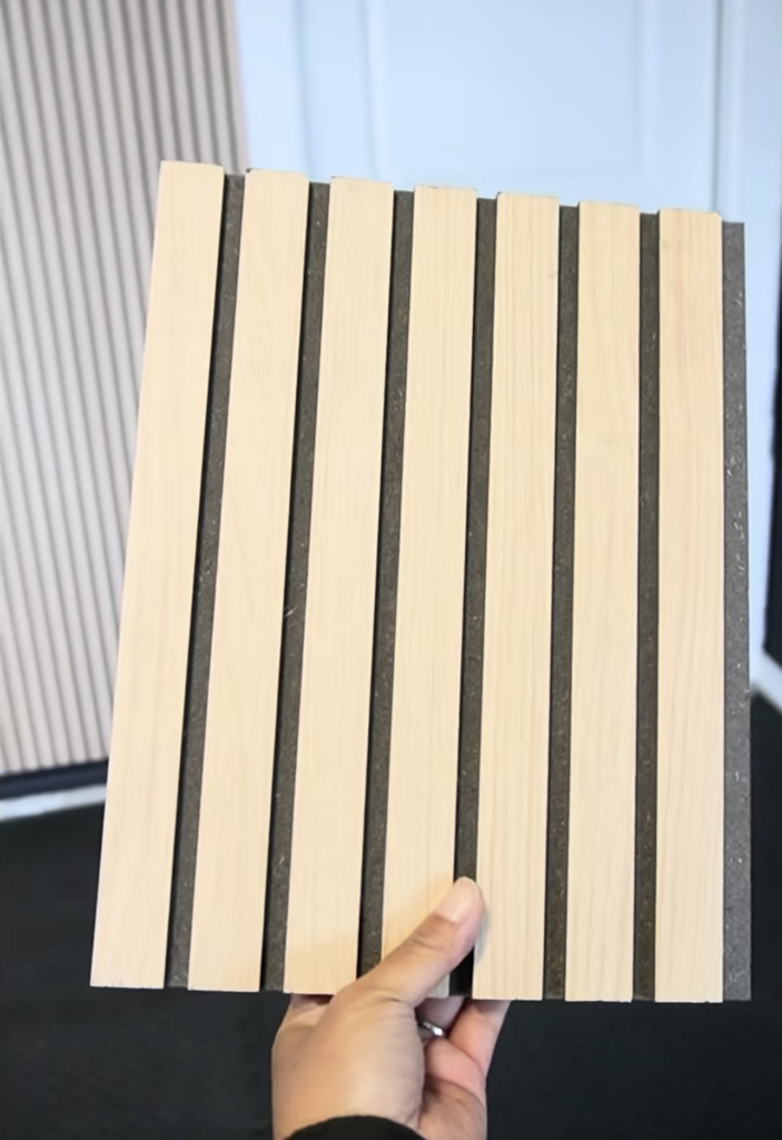 Close-up of a fluted MDF wall panel from Lowe's showing warm oak finish and deep black slat detail