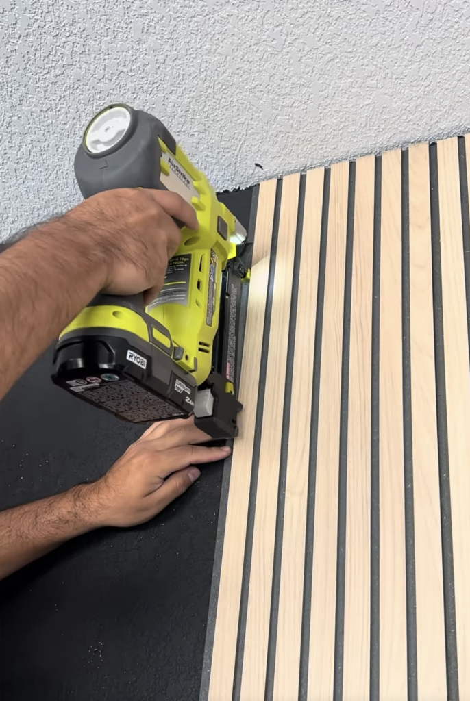 Ryobi brad nailer being used to nail fluted MDF wall panel to wall during accent wall installation