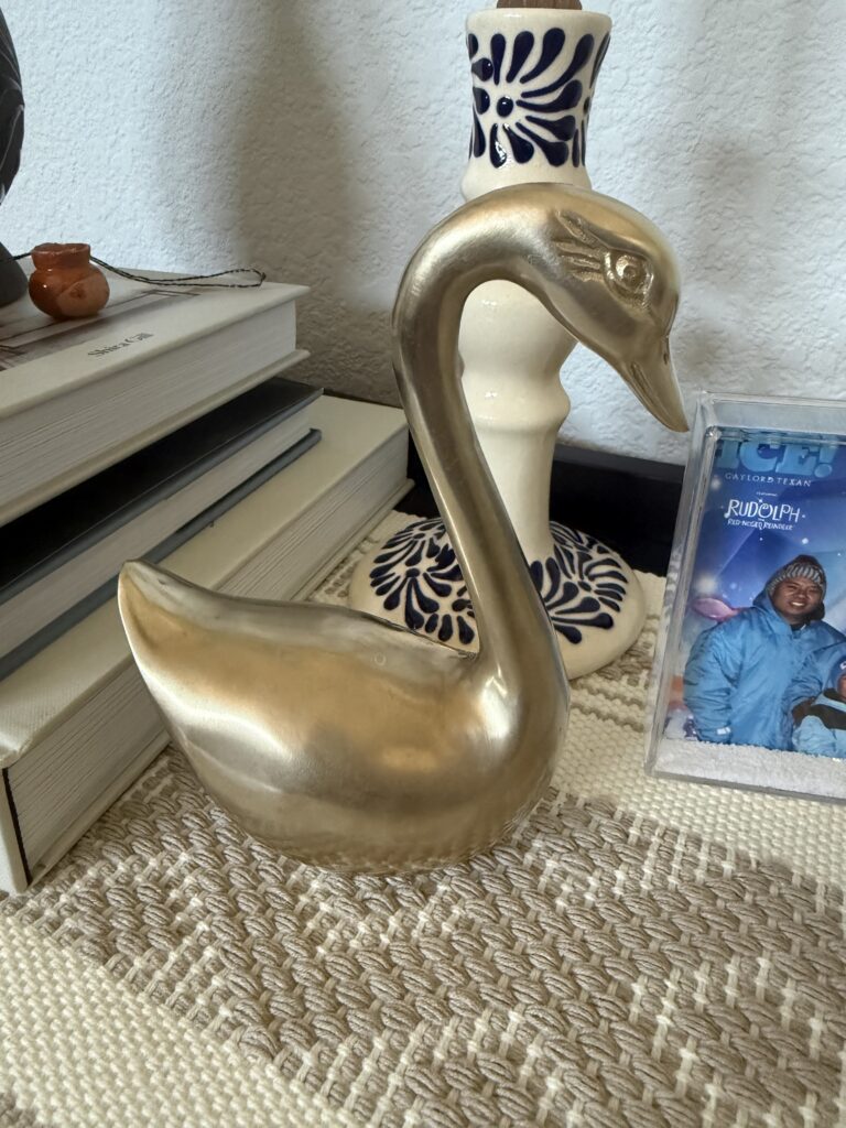 Polished brass swan cleaned with The Pink Stuff paste styled on a woven shelf with stacked books and Talavera pottery
