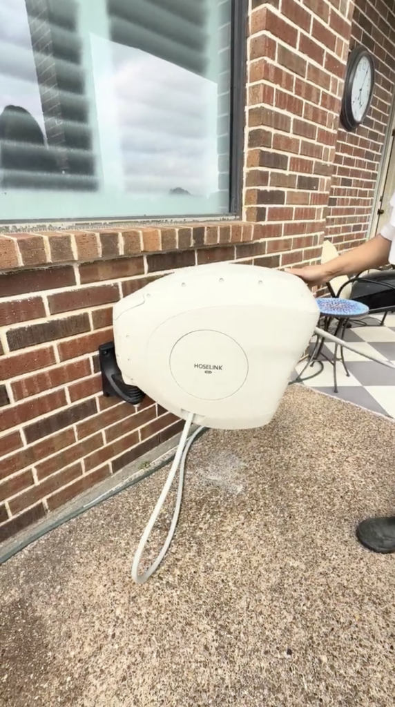 Beige Hoselink retractable hose reel wall mounted on brick exterior with hose extended