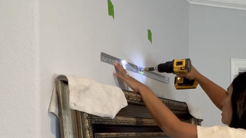 Adriana from Texas DIY Mama installing an Ook French cleat bracket on drywall using a DeWalt drill and a bubble level over painter's tape stud markings